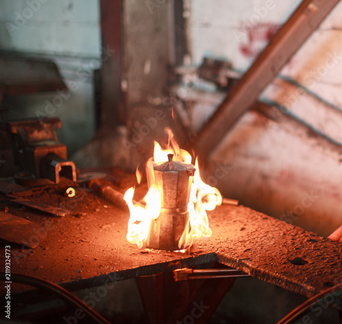 Canvas Print Vintage Moka pot espresso maker engulfed in bright flames on a metal workbench i