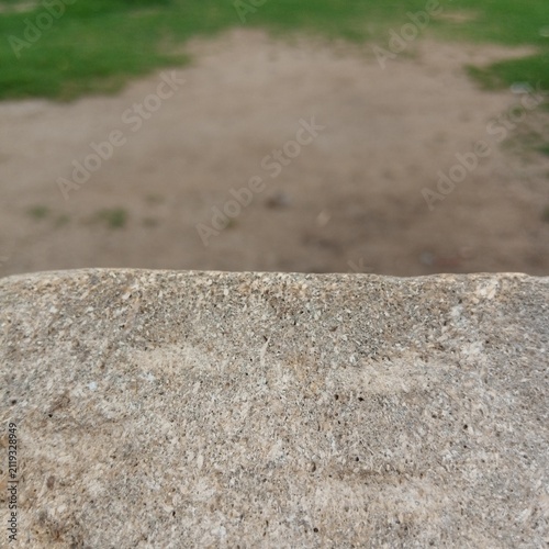 Rough grey concrete stone ledge edge sharply in focus in the foreground with a completely blurred dirt ground behind it