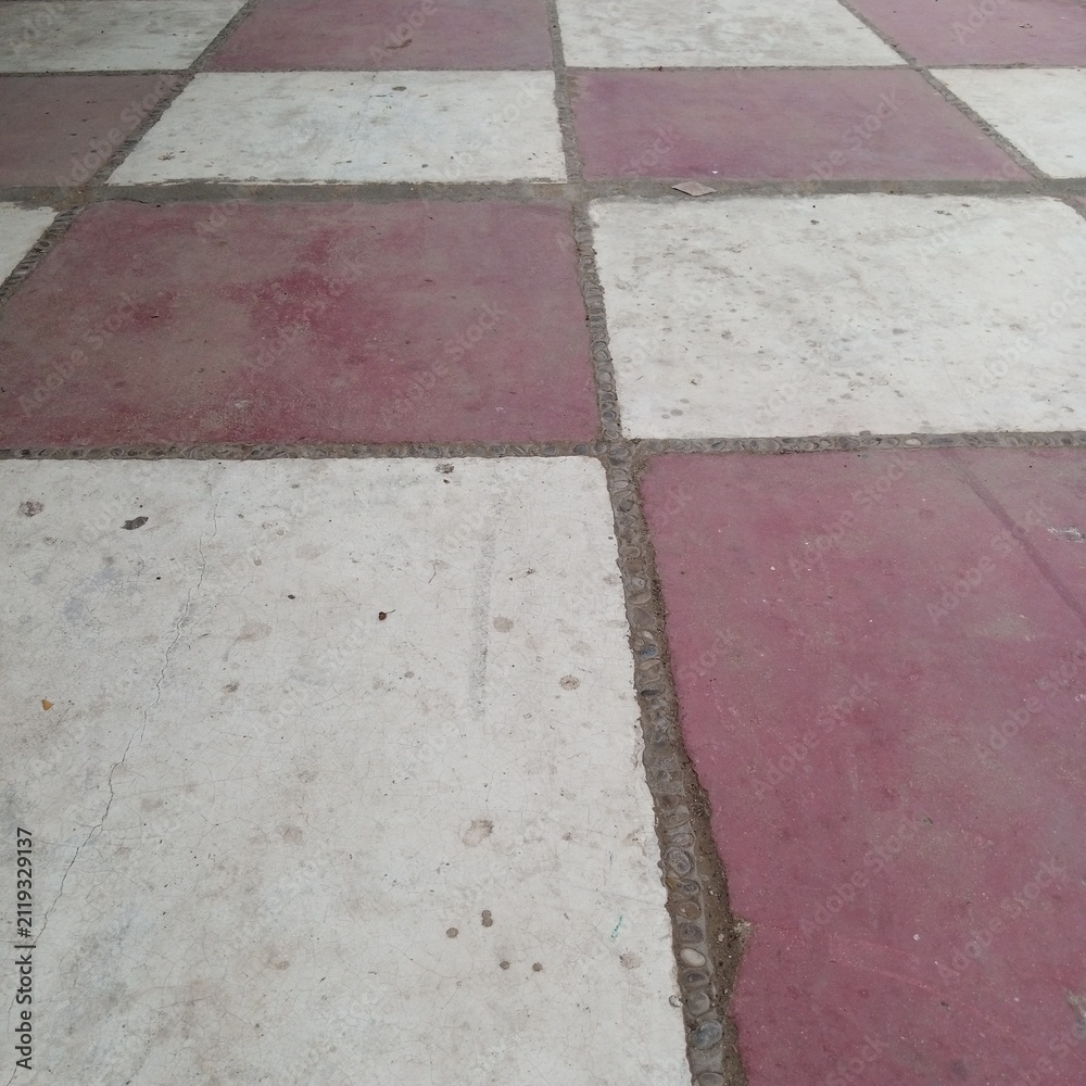 Fototapeta premium Classic alternating checkerboard pattern outdoor courtyard floor tiles painted in faded red and white contrasting visual colors
