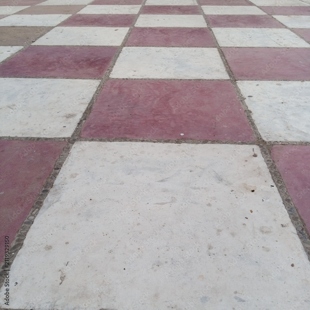 Fototapeta premium Low angle perspective view of a classic red and white alternating checkerboard tiled outdoor courtyard flat floor surface