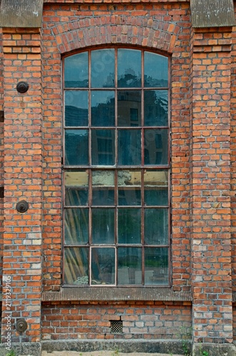 Fotografie Weathered brick factory wall with tall arched industrial window, rusted metal fr