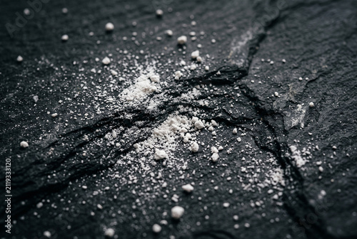 White powder scattered across a rough dark stone surface in macro detail
