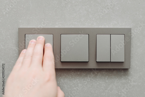 grey light switch attached to wall, minimalistic interior, man hand switching light