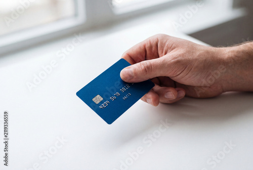 Man holding a plain blue plastic payment card near a bright window