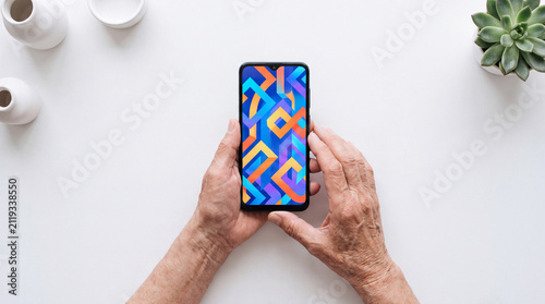 Older hands hold a smartphone showing bright geometric wallpaper on white