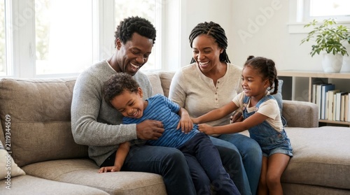 Happy black family of four enjoying quality time laughing and playing together on a comfortable sofa in a bright modern living room