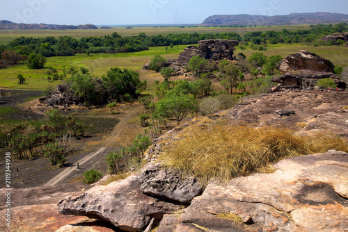 Foto Two hikers traverse the rugged sandstone cliffs overlooking an expansive landscape of green plains and trees