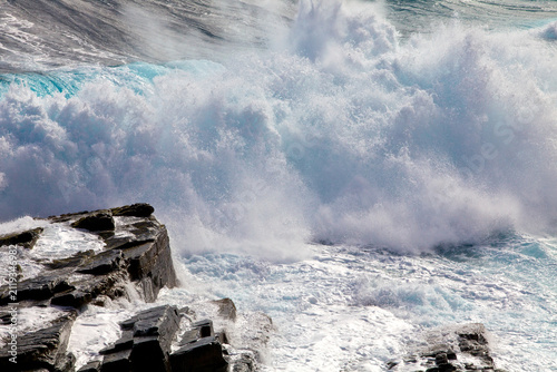 Canvas Print A powerful ocean wave crashes against the dark jagged rocks of the rugged coastline