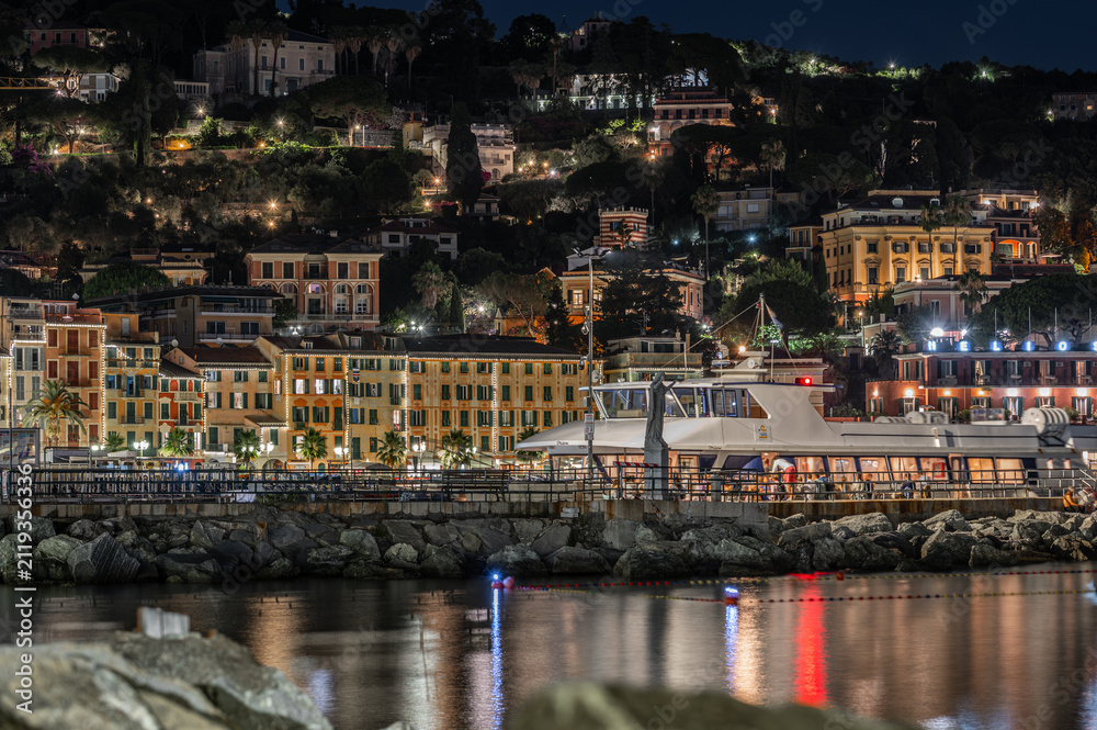 Obraz premium Panoramic night view of illuminated coastal town and hillside houses behind stone breakwater in Santa Margherita Ligure, Italy