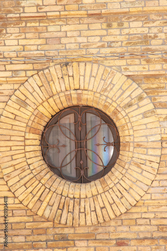 Front view, medium distance of, a yellow brick wall and circular window with decretive iron work, at Fossacesia, bath house, in Italy