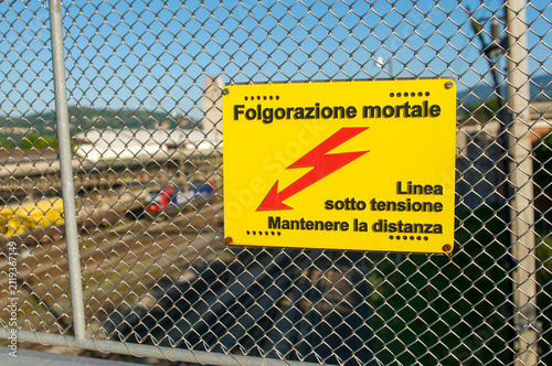 Фотография High voltage danger sign warning of fatal electrocution on railway fence in Chia