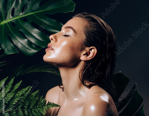 Portrait of a Model with Radiant Wet Skin Surrounded by Green Tropical Leaves