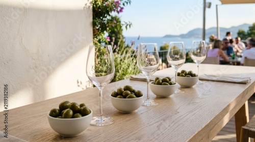 Elegant wine glasses and olives in bowls on a sunlit terrace table, perfect for modern outdoor dining and entertaining with copy space