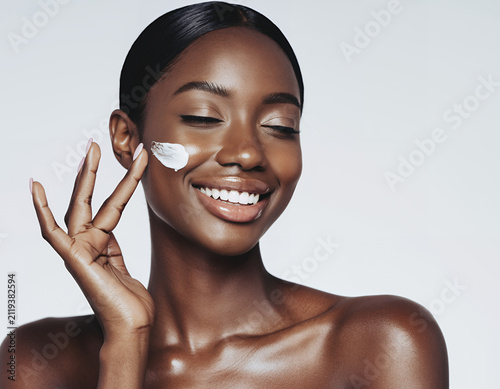Radiant Smiling Woman Applying White Moisturizing Face Cream to Her Glowy Skin