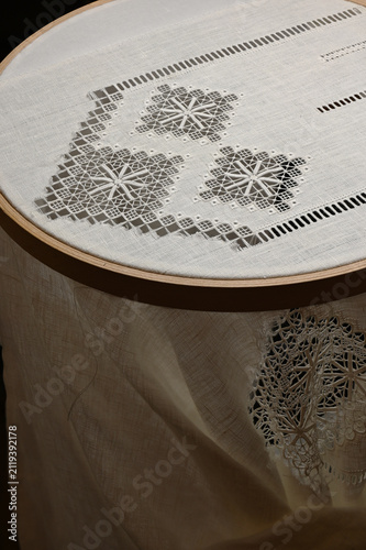 A traditional drawn thread embroidery project on fine linen fabric stretched in a large wooden embroidery hoop