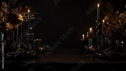 Elegant dark moody dinner table setting with black candles, flickering flames, dried floral arrangements, and sophisticated tableware against minimalist black background