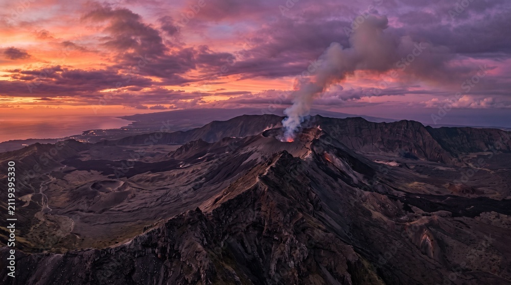 Fototapeta premium Active volcano erupts at sunset, dense smoke and ash rising into a dramatic twilight sky over rugged mountains, a powerful display of nature