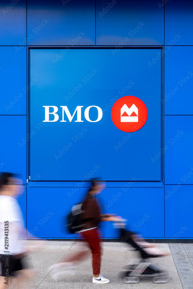 Fototapeta premium Toronto, Canada - June 19, 2026: Pedestrians passing BMO bank logo on blue building exterior