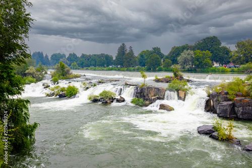 Scenic view of the Snake River flowing through Idaho Falls, Idaho, featuring peaceful river waters, cascading waterfalls, lush green riverbanks, and the natural beauty of eastern Idaho. 