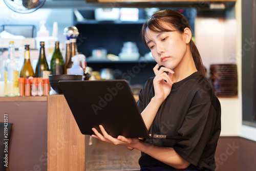 居酒屋で困った顔をしながらパソコンを使う女性店長