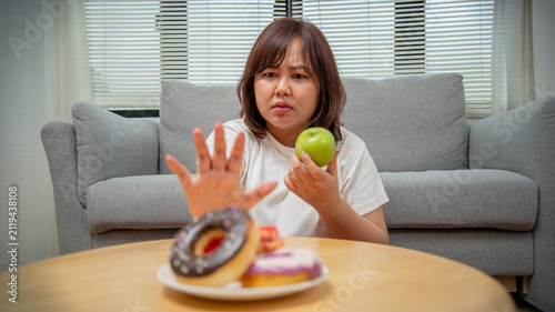 Overweight teenage girl rejecting sweets and choosing fruit for healthy eating, weight loss, obesity prevention, nutrition, and wellness concept.