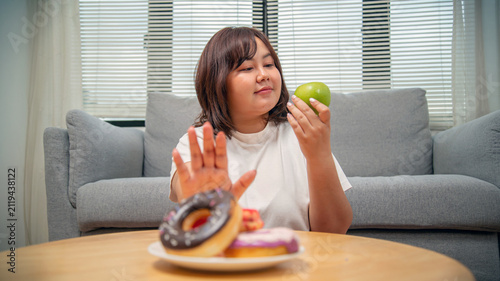 Overweight teenage girl rejecting sweets and choosing fruit for healthy eating, weight loss, obesity prevention, nutrition, and wellness concept.