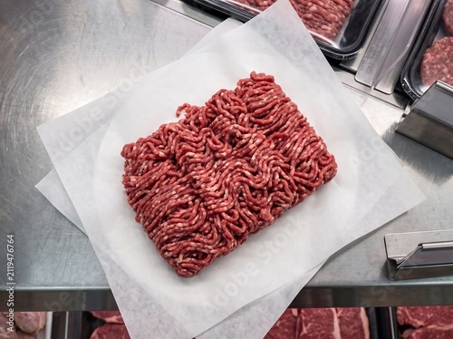 Fresh ground beef on white parchment paper at a local butcher shop area.