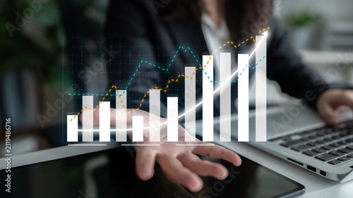 A business professional engages in extensive financial analysis using virtual graphs, showcasing growth trends and strategic insights in a modern office environment. Impute