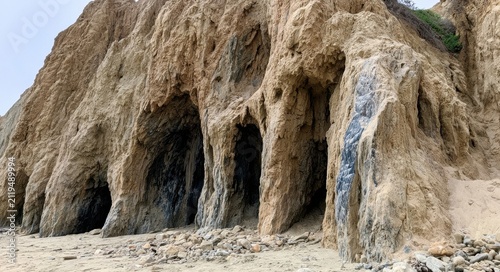 Coastal cliff with eroded caves and sandy beach foreground