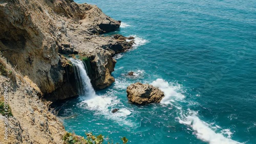 Stunning natural waterfall flowing from a rocky cliff into the turquoise sea.