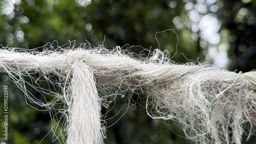 Frayed white rope strands with a knot against a blurred green outdoors