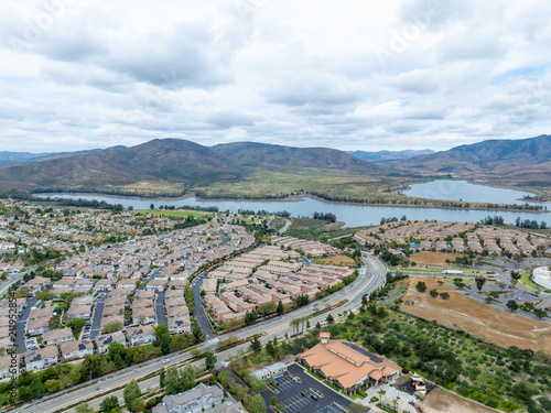 An aerial view of a large housing community near Otay Lakes in Chula Vista featuring dense suburban single-family blocks, winding green parkways, and close proximity to the Lower Otay Lake reservoir