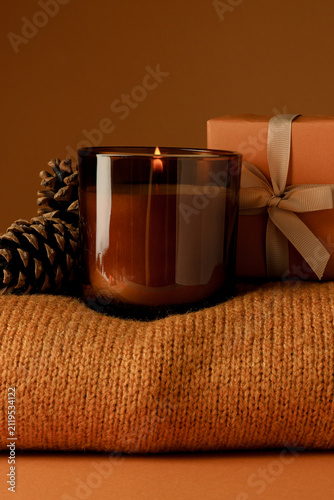 Candle, cones and box on sweater on orange background