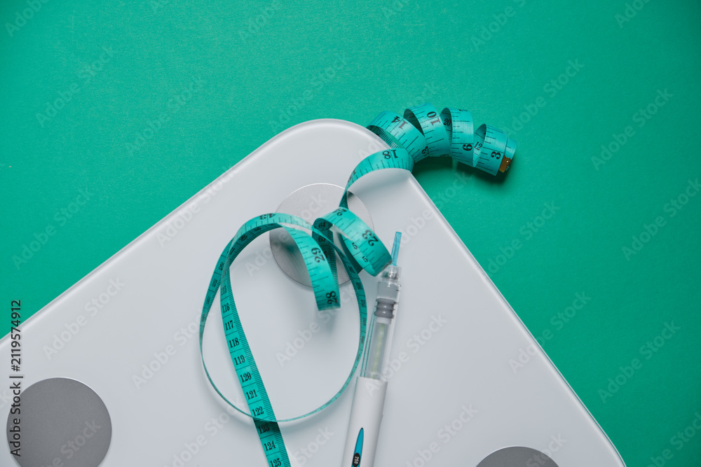 Fototapeta premium Glp-1 injection pen with a measuring tape on a weight scale providing a concept of weight loss treatment