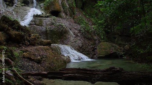 A waterfall with clear blue water, surrounded by natural rock formations and lush trees.