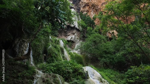 A waterfall with clear blue water, surrounded by natural rock formations and lush trees.