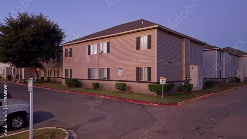 Evening dusk shot of a corner multifamily housing building with parked cars, street sign, and fading sunset light.