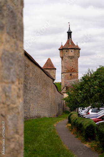 Medieval tower and wall with cars parked nearby.