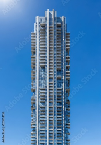 Sleek urban residential tower showcasing transparent glass balconies and minimalist facade design against a clear blue sky during daylight, block, housing, window