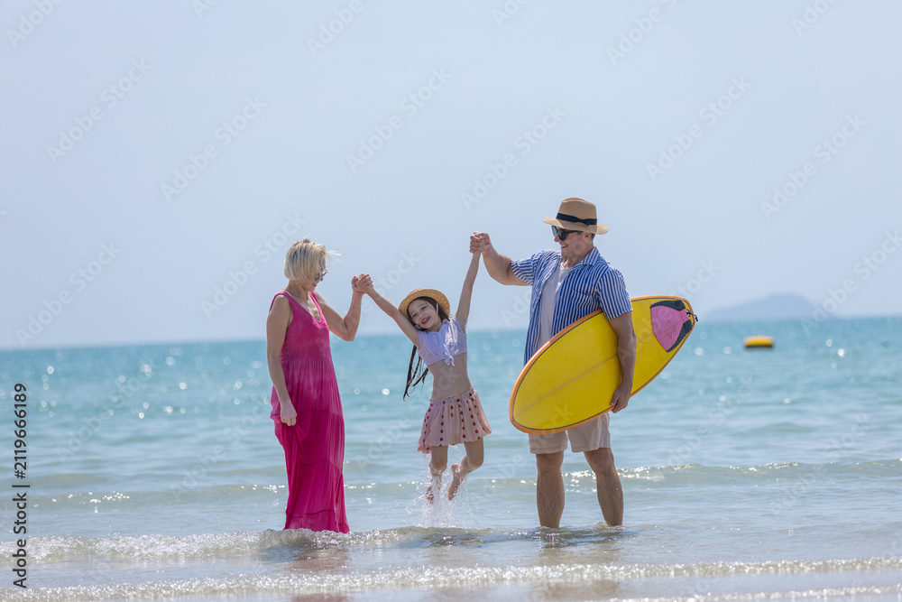 Obraz premium Happy senior family enjoying sunny summer vacation beautiful ocean beach with young child holding hands lifting her with joy carrying yellow surfboard walking shallow water feeling wonderful