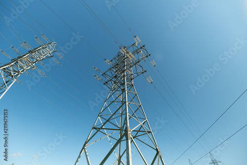 High voltage transmission towers crowded with starlings swirling among power lines against clear blue sky, viewed from low angle with strong sense of height, scale, motion and contrast