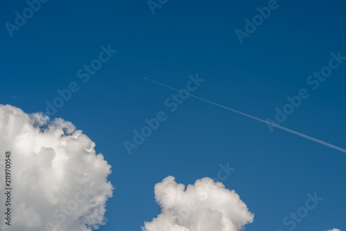 Deep blue sky with white cumulus clouds and high altitude jet contrail