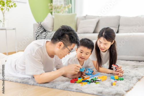 фотографія An Asian family of three plays with colorful toys together on a soft carpet in a bright, cozy indoor home setting