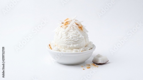Coconut ice cream scoop with shaved and toasted coconut in white bowl