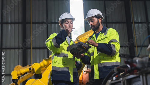 Two engineers discussing industrial robot performance and reviewing inspection information during a maintenance evaluation inside an automated factory.