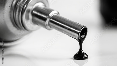 Close-up of black viscous liquid dripping from a metal nozzle, isolated on white background