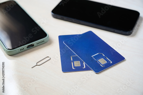 Two sim cards lying on a table, dark smartphones and paper case. Replacing SIM cards for a smartphone.