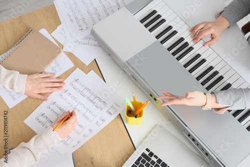 Hands of teenage boy learning music notes with teacher playing synthesizer on...