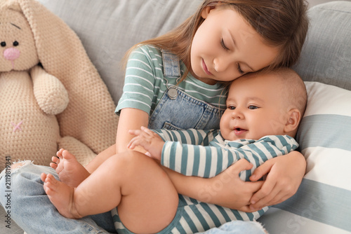 Little girl hugging her baby brother on sofa at home