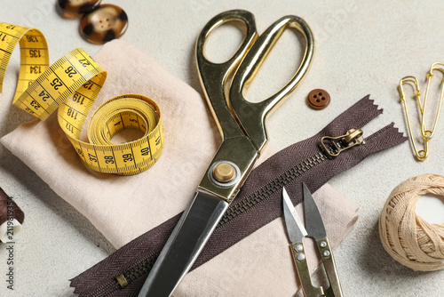 Different tailors supplies with measuring tape and beige cloth on grunge white background